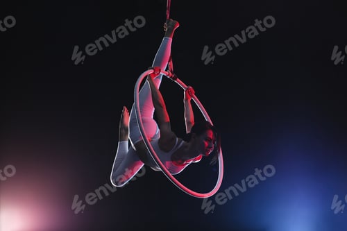 Preview: Young woman performing acrobatic element on aerial ring against dark background