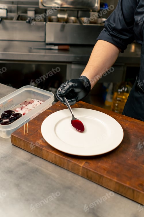 Preview: in professional kitchen with a chef wearing black gloves red sauce in a spoon plate decoration