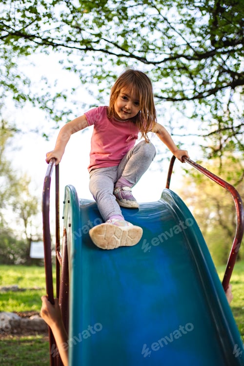 Preview: Joyful child climbing down a colorful slide in a sunny park