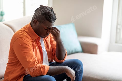 Preview: Tired black man sitting on couch at home, copy space