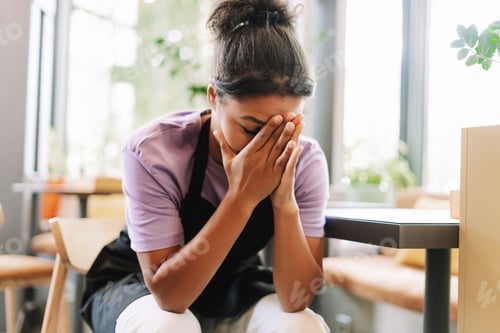 Preview: Young, unhappy African American tired waitress covering her face with hands in a restaurant