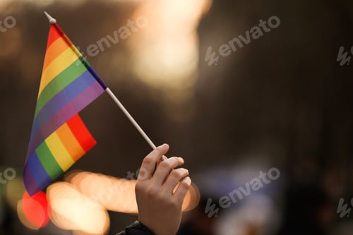Preview: Woman holding small LGBT flag on city street, closeup. Space for text