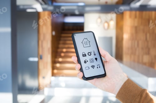 Preview: man controls smart home devices using app for mobile phone on background of interior of house.