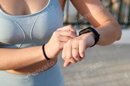 Preview: Close-up fitness woman looks at her electronc watch outdoors