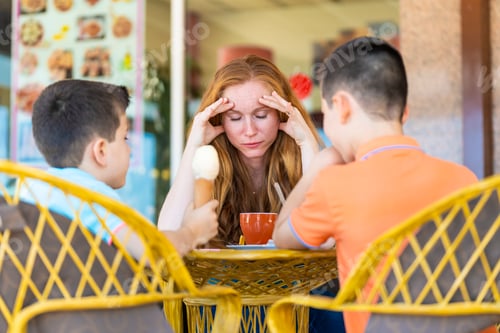 Preview: Stressed mother on a terrace of a coffee shop with her two children