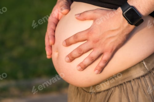 Preview: Close-up view of the hands of a man on the abdomen of a pregnant woman outdoors