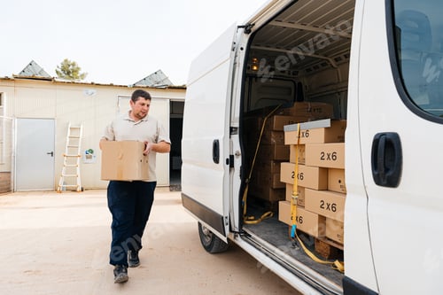 Preview: Focused young man walking near parked van with carton box in hands