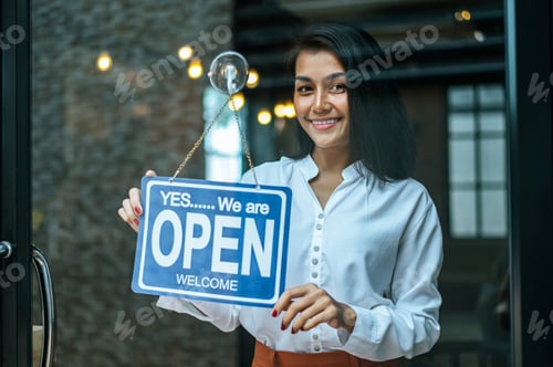 Preview: woman stands and opens a wide sign through the shop window and smile.
