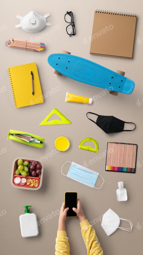Preview: Top view of child with smartphone and school supplies, distance learning and coronavirus concept.