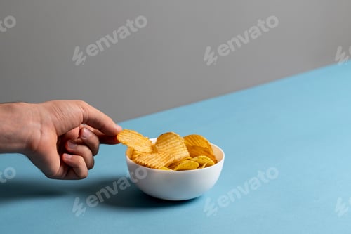 Preview: simple concept of junk food, hand pick a single potato chip from bowl