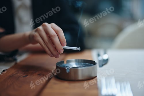 Preview: A woman with a cigarette in her hands shakes the ashes into an ashtray, close-up