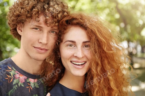 Preview: Confident red-haired guy in floral design t-shirt standing close to his attractive girlfriend with f