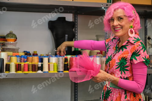 Preview: Seamstress with pink hair smiling and looking at camera choosing a thread.