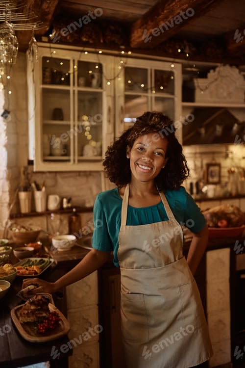 Preview: Happy black woman cooking family meal for Thanksgiving in the kitchen and looking at camera.