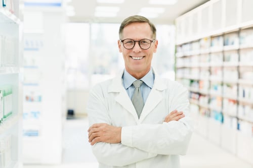Preview: Druggist in white medical coat standing with arms crossed in pharmacy drugstore