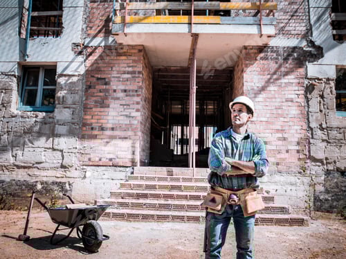 Preview: A bricklayer equipped with various tools poses in front of a house under construction.