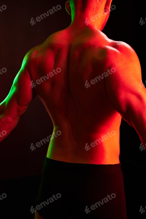 Preview: Man bodybuilder athlete with naked torso in sports uniform, isolated on black background in neon