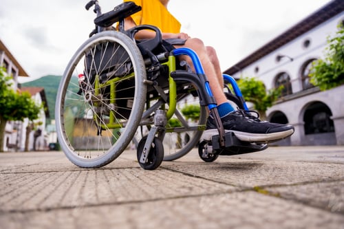 Preview: Detail of a disabled person in a wheelchair walking through the town square