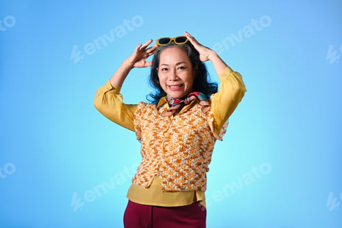 Preview: Cool and stylish asian senior woman with sunglasses and fashionable clothes on light blue background