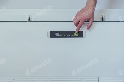 Preview: Man's hand changes the temperature in a large white air conditioner, close-up photo