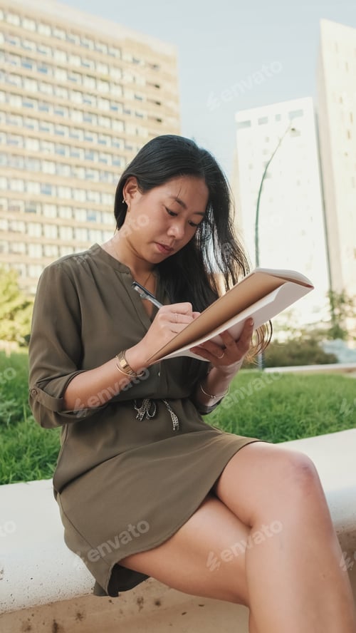Preview: Young girl looks through notes in notebook while sitting on modern buildings background