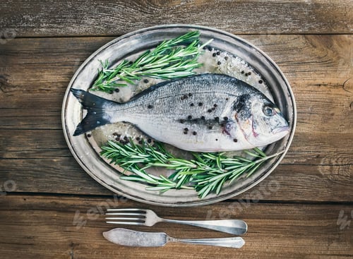 Preview: Fresh sea fish (sea bream) on a metal dish with rosemary and spi