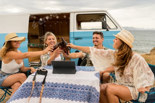 Preview: Friends sitting next to a van and toasting with beer