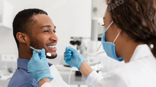 Preview: Young african guy smiling to his female dentist
