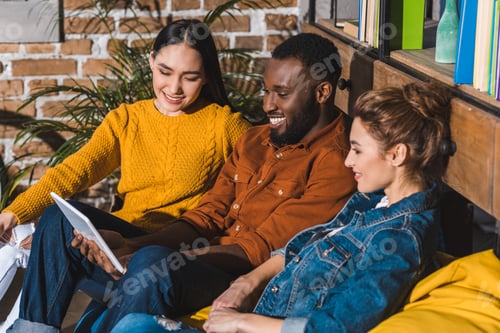 Preview: happy young multiethnic friends using digital tablet together at home