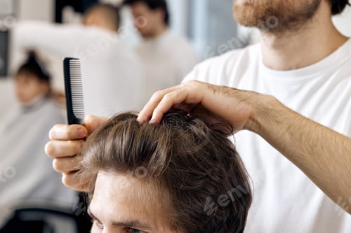 Preview: close-up, professional male hairstylist combing young customer's hair