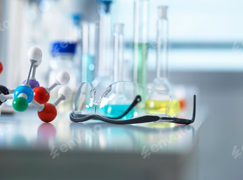 Preview: Safety glasses and molecular model on laboratory bench, scientific equipment in background