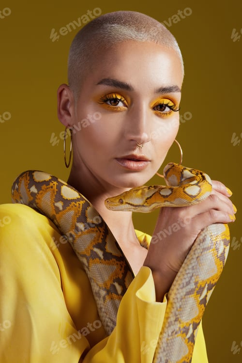 Preview: Shot of a fashionable woman holding a snake while modelling a yellow concept