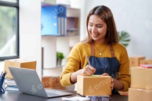 Preview: Happy young Asian business owner woman prepare parcel box and check online orders of product for del