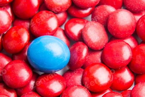 Preview: Focus on blue chocolate candy against heaps of red candies