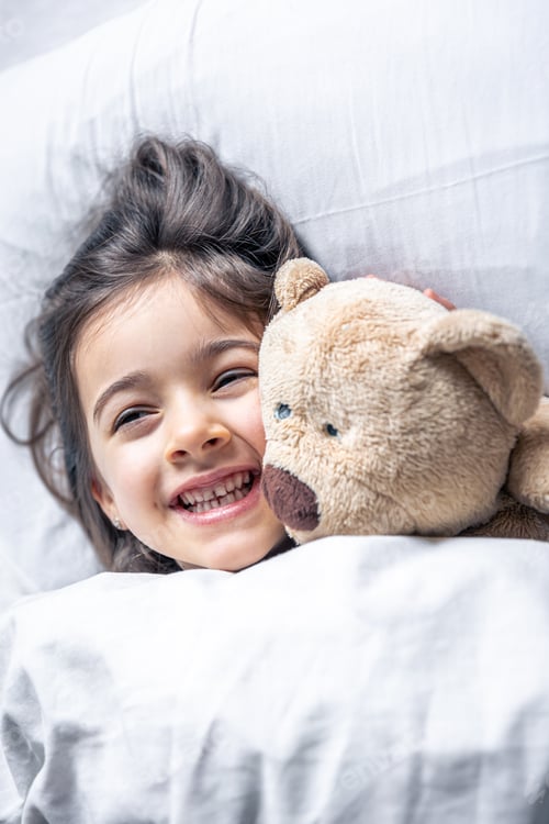 Preview: Little cute girl in bed with a teddy bear early in the morning.