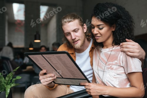 Preview: Portrait of young beautiful couple sitting in restaurant with menu in hands