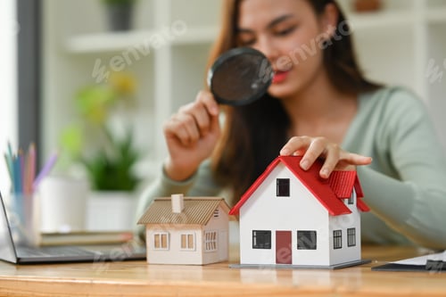 Preview: Female appraiser looking at house model through magnifying glass.