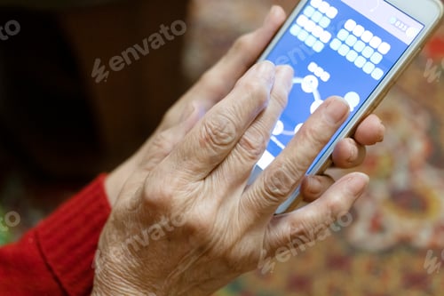 Preview: hand of old woman playing on smartphone in evening