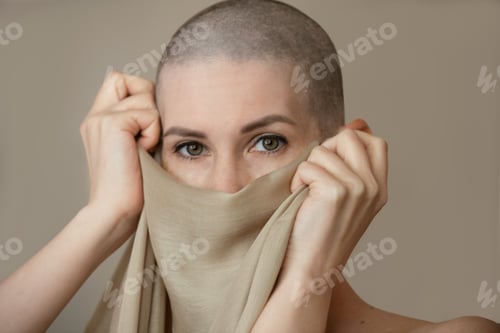 Preview: Young slender woman after chemotherapy without hair on her head covers her face and mouth with a