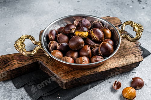 Preview: Cracked roasted chestnuts served in a skillet. Gray background. Top view