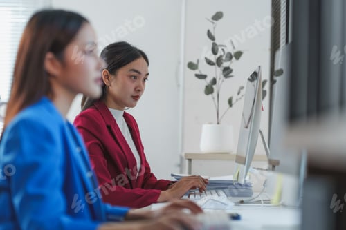 Preview: Two professional women concentrate on tasks at their computers in a contemporary office setting, sho
