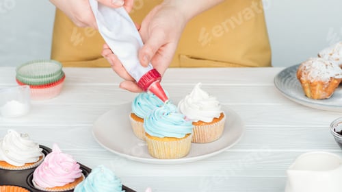 Preview: partial view of woman decorating cupcakes with icing bag