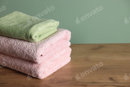 Preview: Stack of clean towels on wooden table against green background, closeup. Space for text