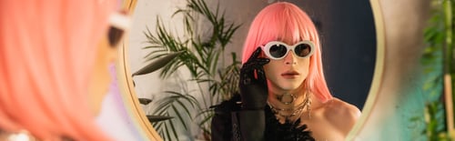 Preview: Fashionable drag queen in pink wig wearing sunglasses near mirror at home, banner