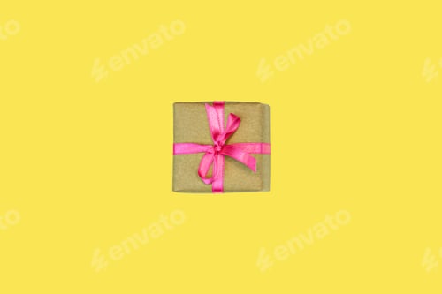 Preview: flatlay of single present gift box with pink ribbon isolated on yellow background top view