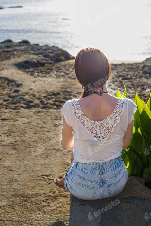 Preview: back view of a girl sitting on sandy beach alone on the sea background