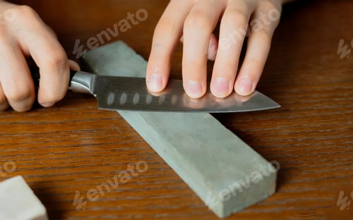 Preview: young man sharpening a knive on wooden table on dark background b