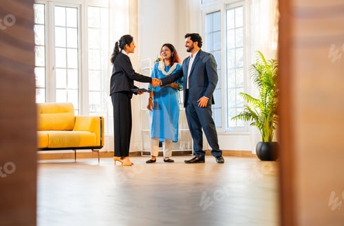Preview: Handshake between Indian woman real estate agent or architect and young married couple in home