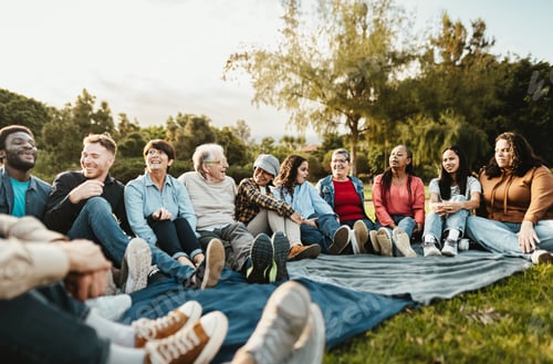 Preview: Happy multi generational people having fun sitting on grass in a public park
