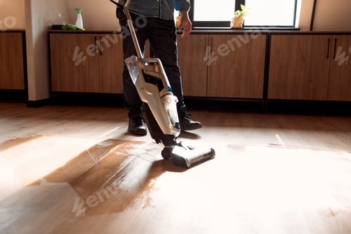 Preview: man vacuuming wooden floor in loft iving room with vacuum cleaner. Close up